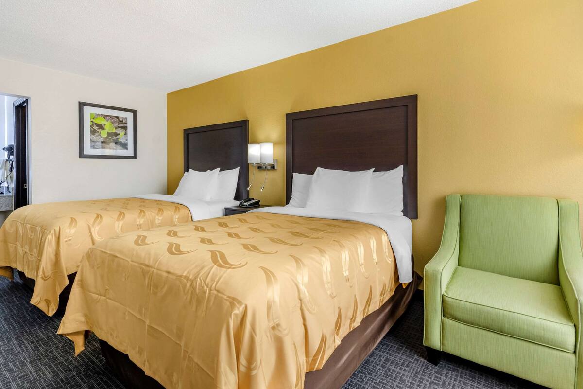 A hotel room with two beds, a green armchair, and a framed picture on the wall.