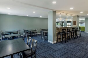 Un comedor moderno con varias mesas y sillas, una zona de bar con taburetes y una cocina al fondo.