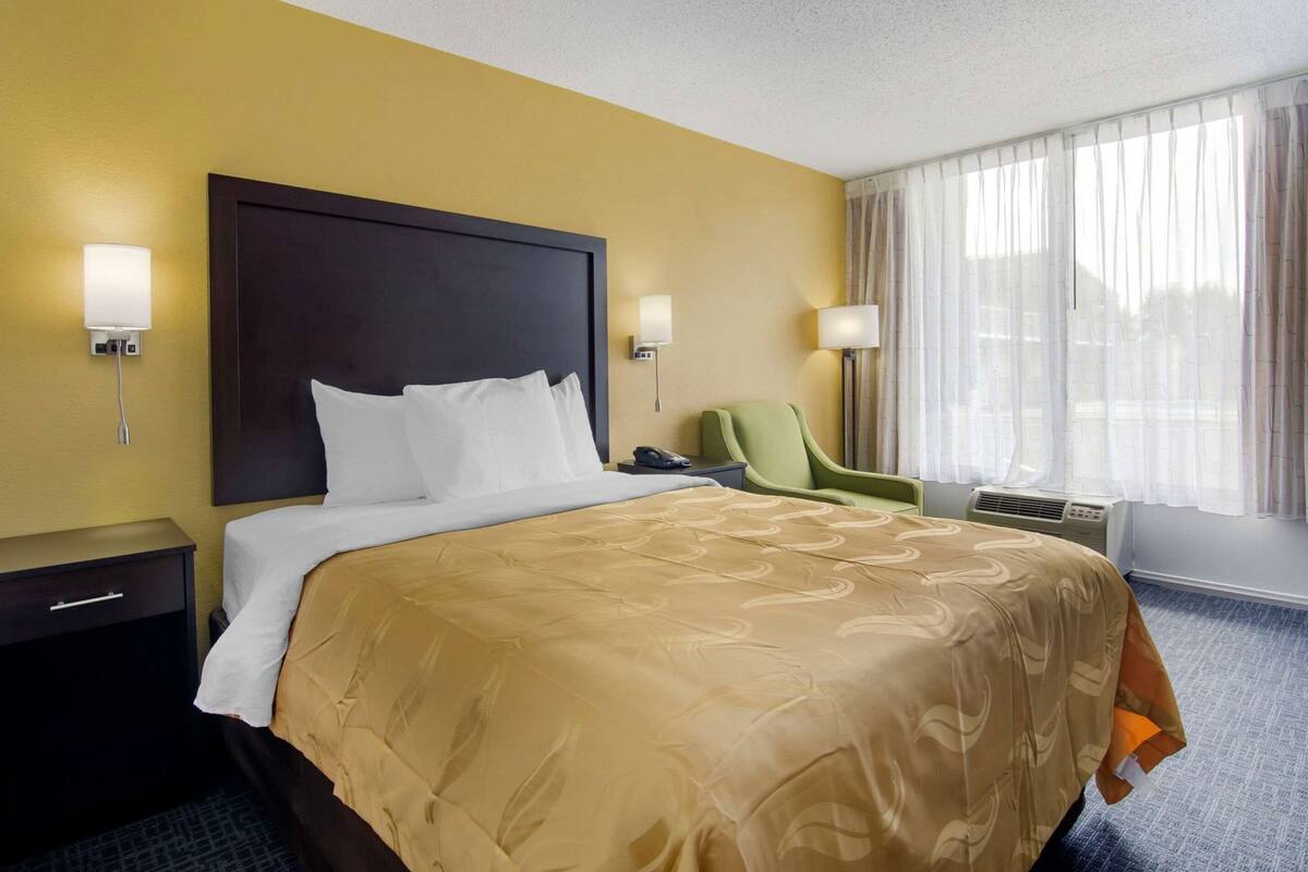 A hotel room with a large bed, bedside tables, a chair, a desk, and a window with curtains.