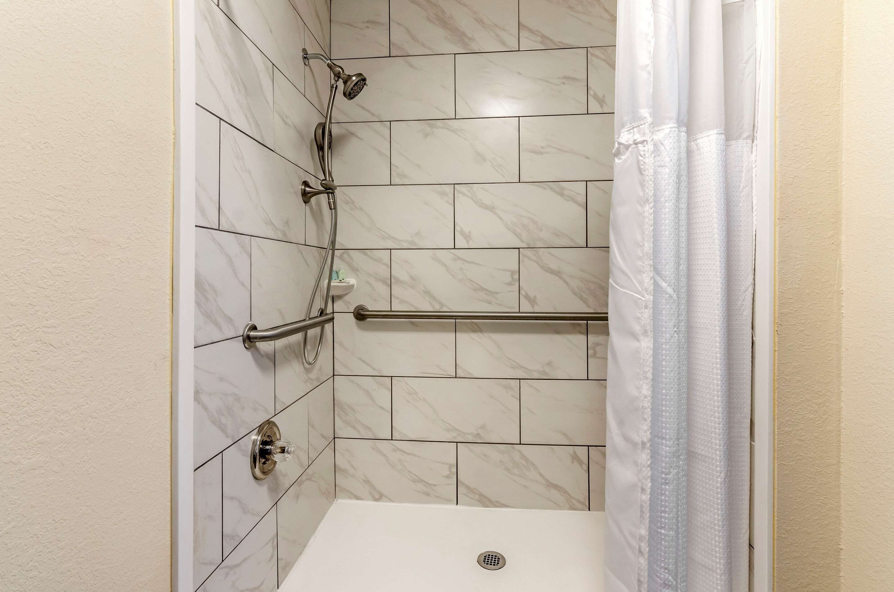 A shower area with a handheld showerhead, a handheld showerhead, and a handheld showerhead.