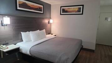A hotel room with a bed, bedside table, lamp, and two framed pictures on the wall.
