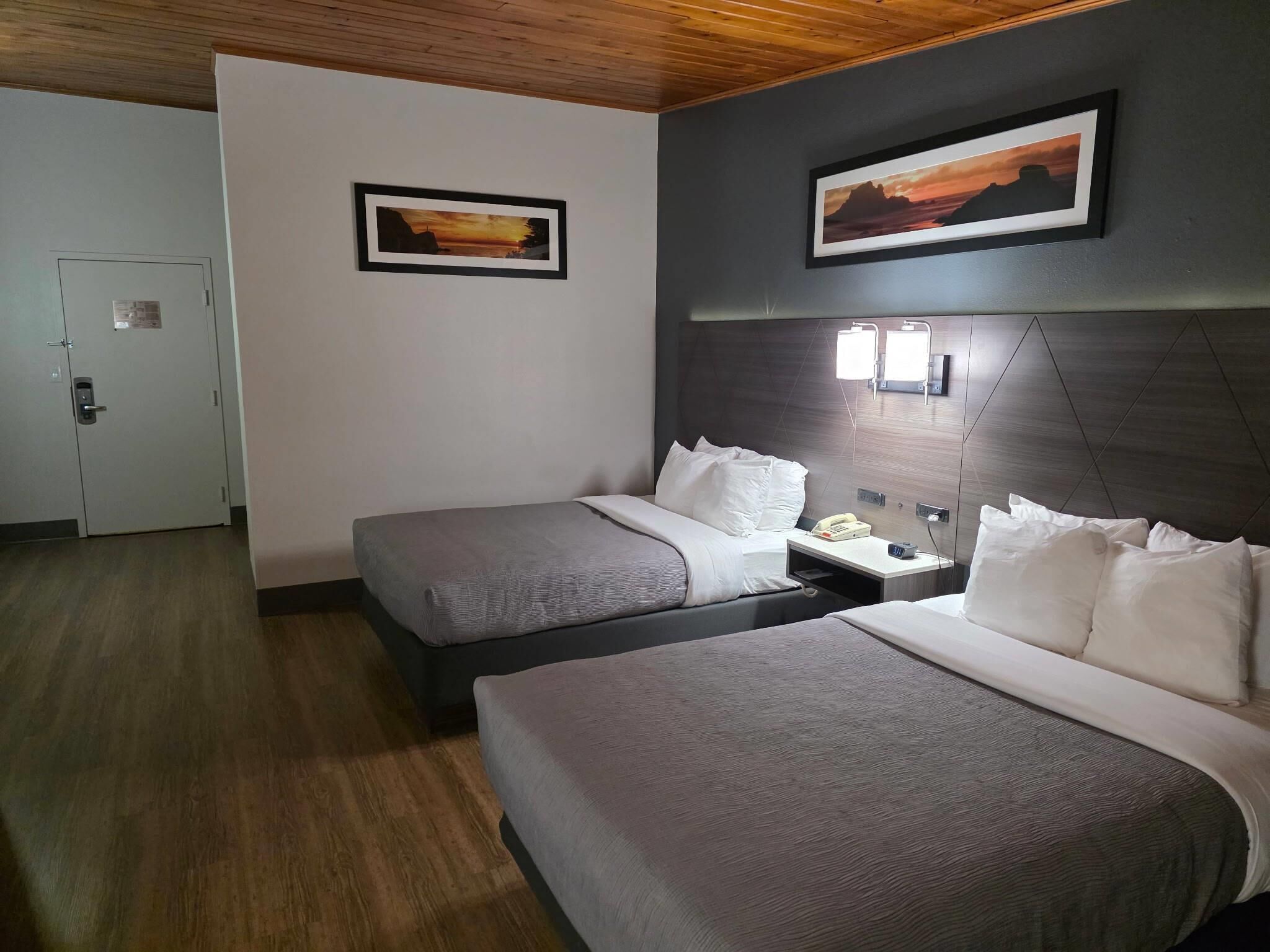 A hotel room with two beds, a wooden ceiling, and two framed pictures on the walls.