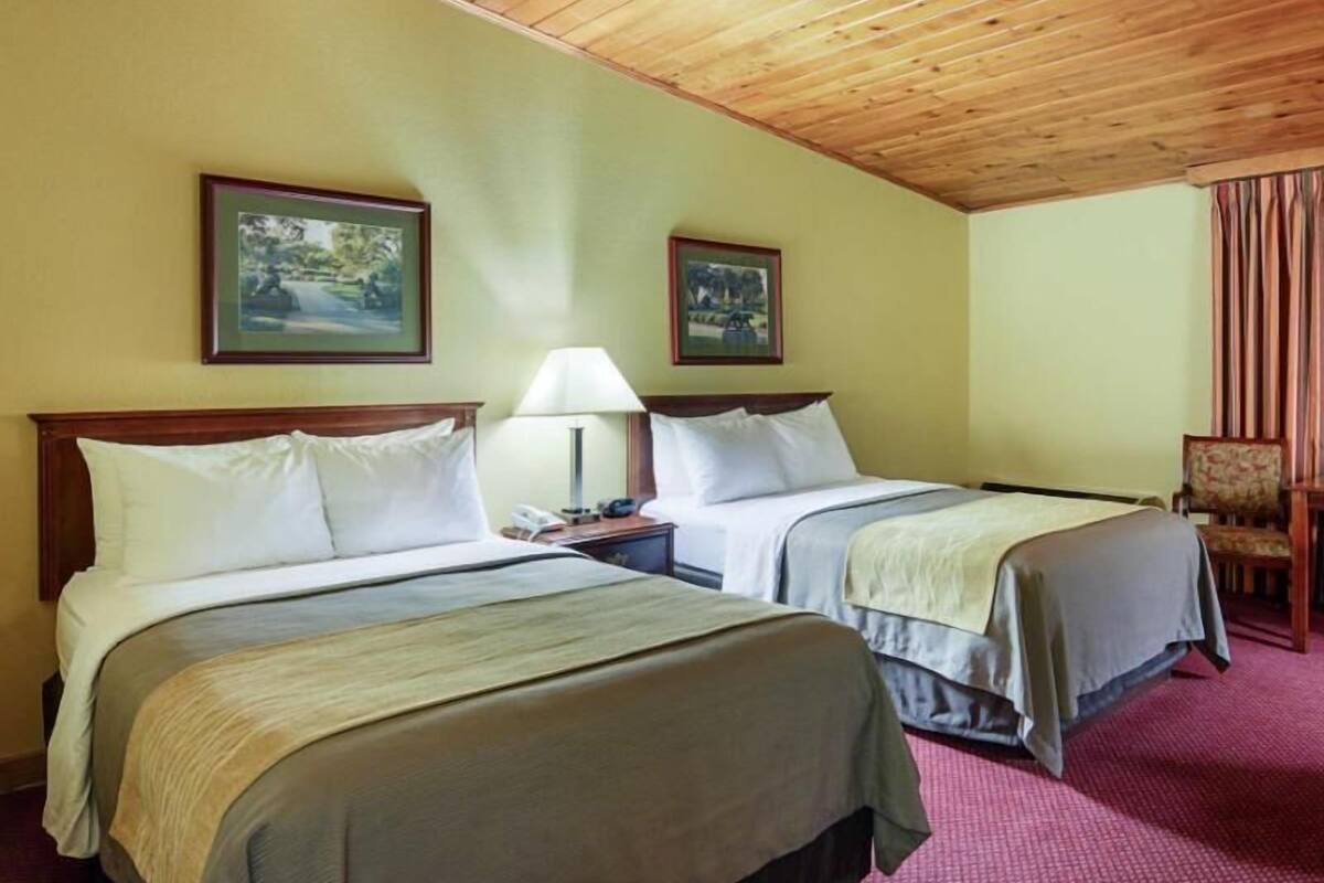 A hotel room with two beds, wooden ceiling, and two framed pictures on the wall.