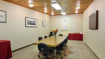 A conference room with a wooden table, black office chairs, a red tablecloth, framed pictures on the wall, and a clock.