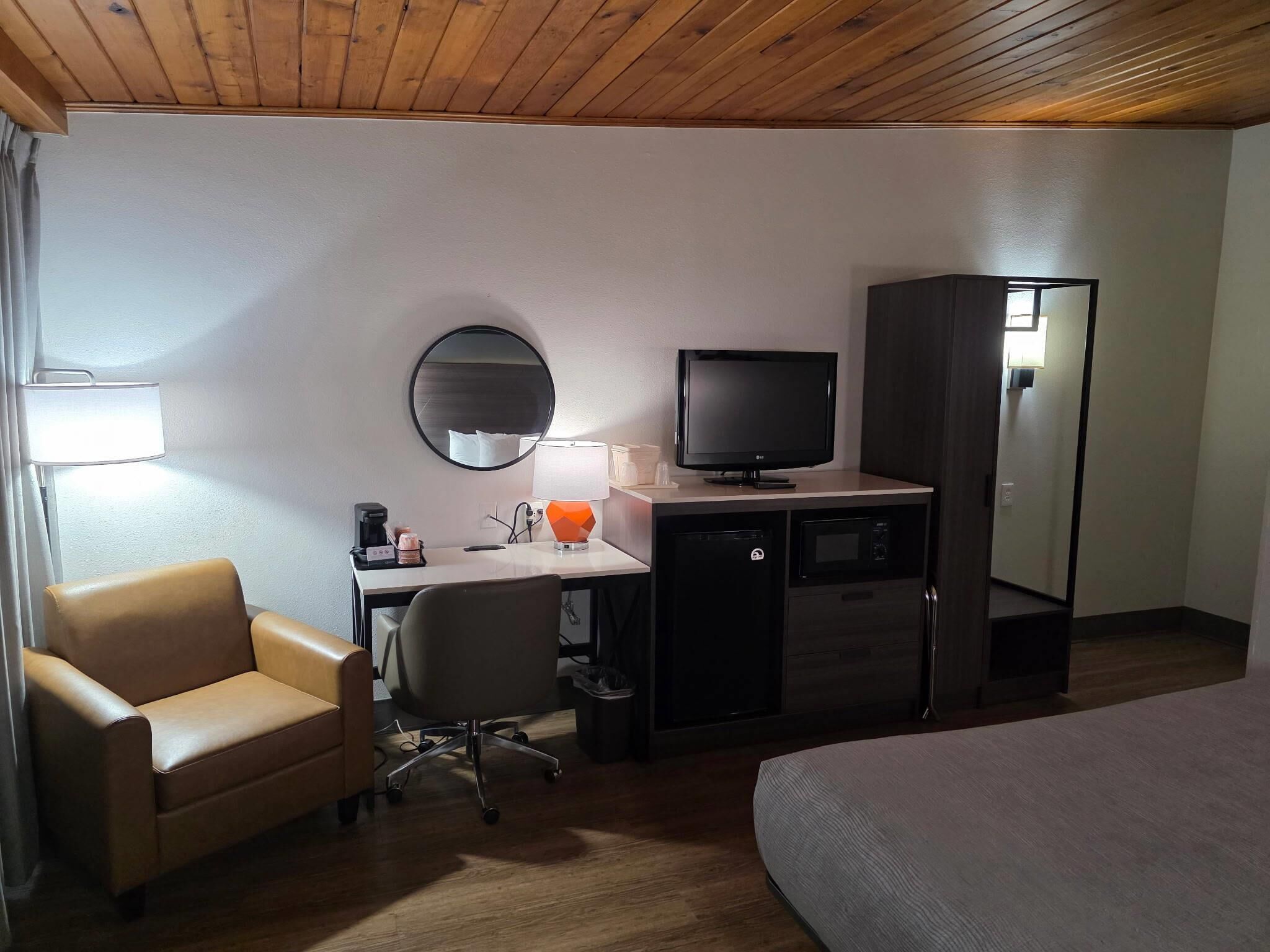 Een hotelkamer met een bed, een bureau met een computer, een televisie, een stoel, een lamp en een spiegel.