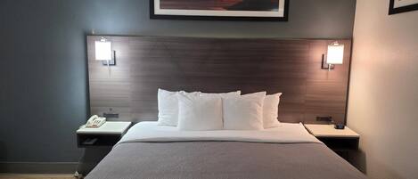 A hotel room with a large bed, two bedside tables, a mounted picture, and a wall-mounted light fixture.