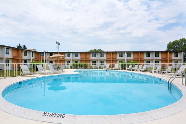 A swimming pool with lounge chairs and a 'NO DIVING' sign, surrounded by a building with multiple windows and a fenced area.