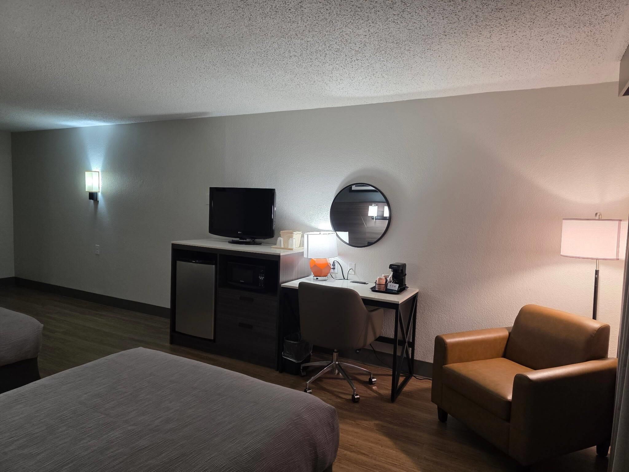 A hotel room with a bed, a desk with a computer, a chair, a television, and a mirror.