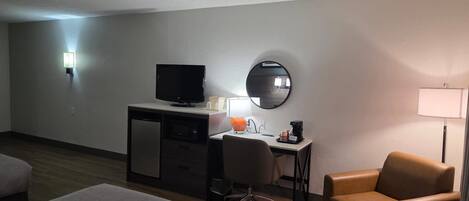 A hotel room with a bed, a desk with a computer, a chair, a television, and a mirror.