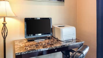 A hotel workspace with a desktop computer, printer, and a lamp.