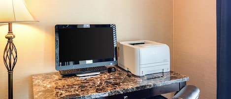 A hotel workspace with a desktop computer, printer, and a lamp.