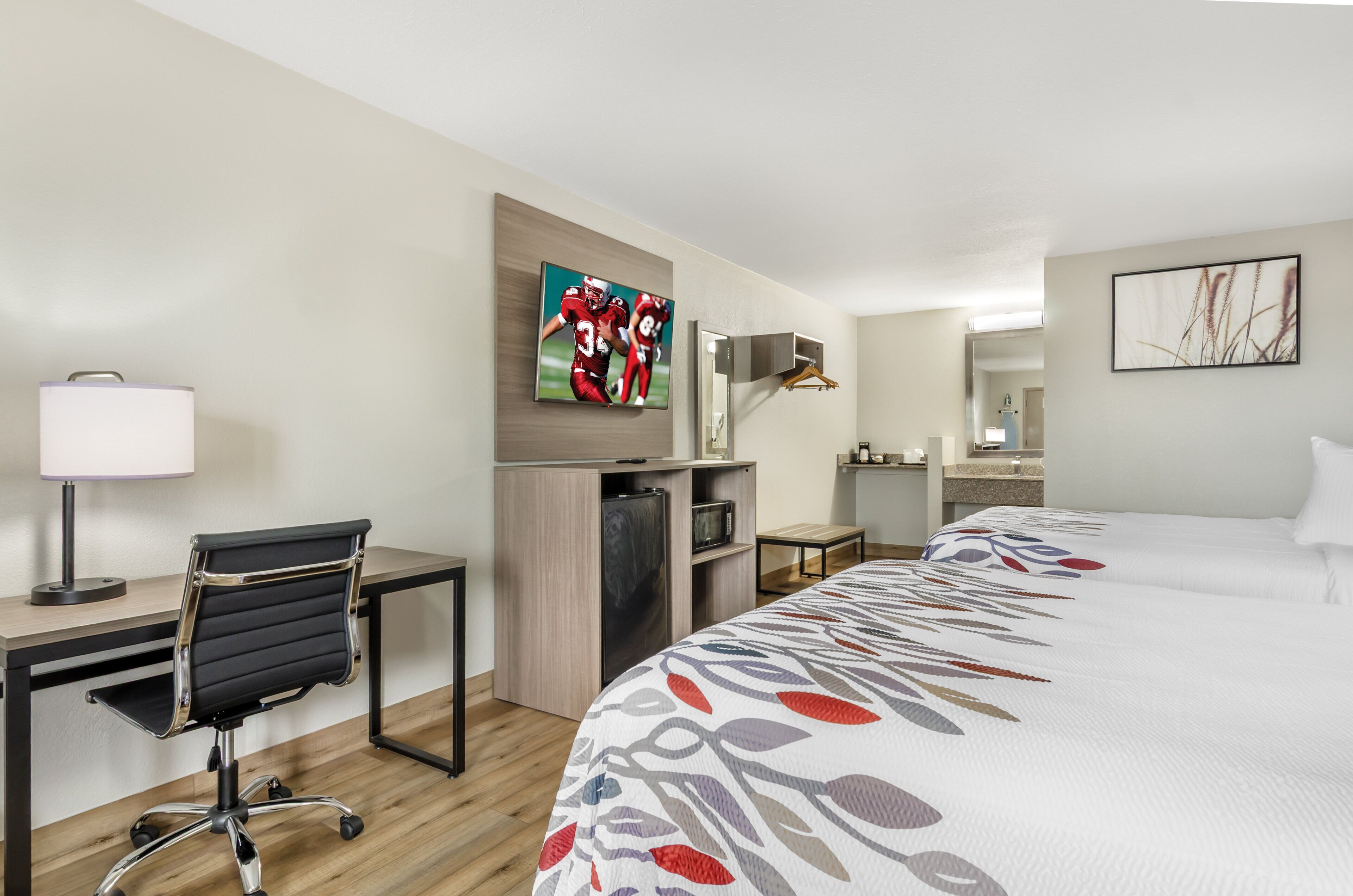 Une chambre d’hôtel avec un lit, un bureau, une chaise et un téléviseur fixé au mur.