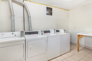 A laundry facility with four Whirlpool washers and dryers, a sign about laundry soap, and a wooden table. - Red Roof Inn Staunton (Staunton)