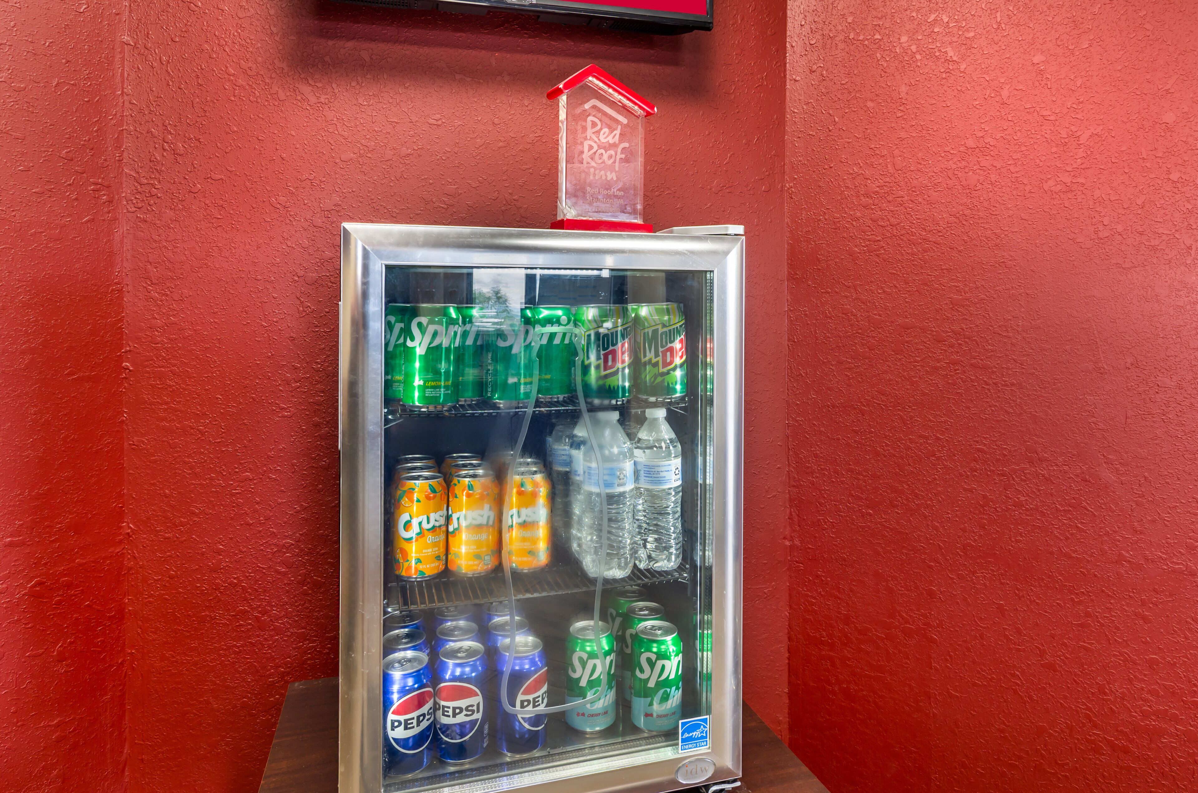 Máquina expendedora con diferentes bebidas, incluyendo Sprite, Crush Naranja y Pepsi, frente a una pared roja.