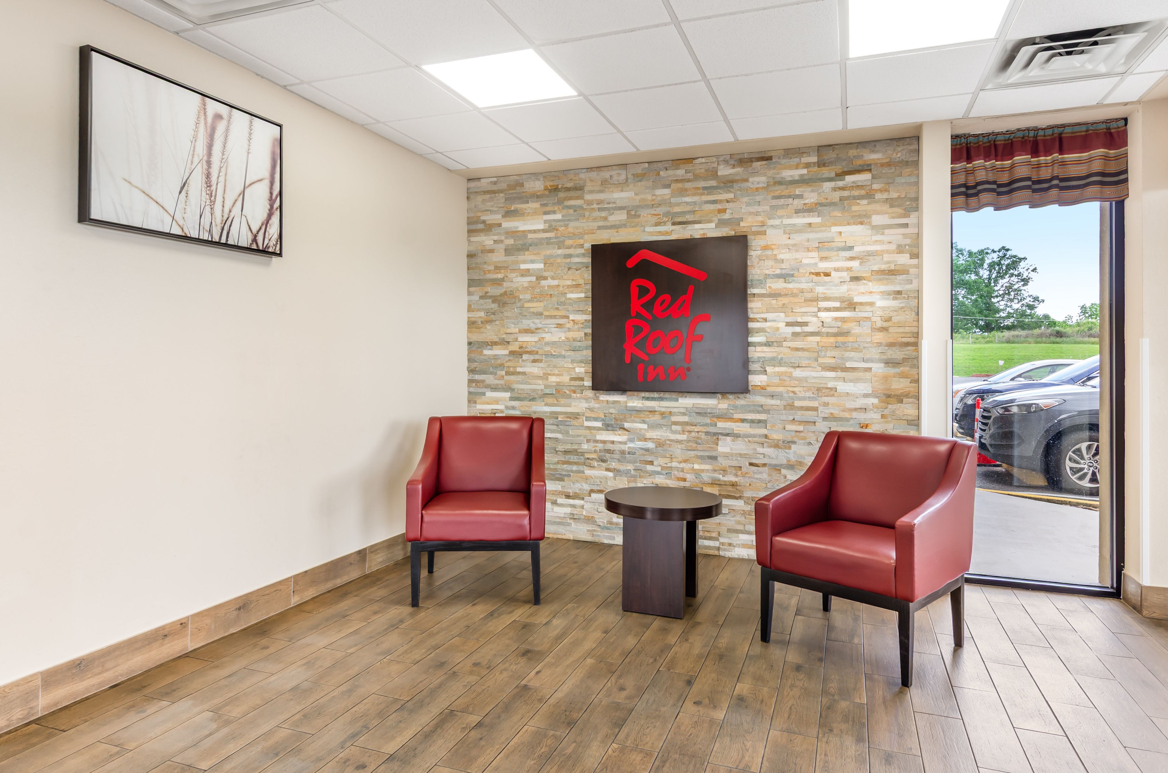 Zona de recepción de Red Roof Inn con dos sillones de cuero rojo, una mesita redonda y una pared de piedra con el letrero de Red Roof Inn.