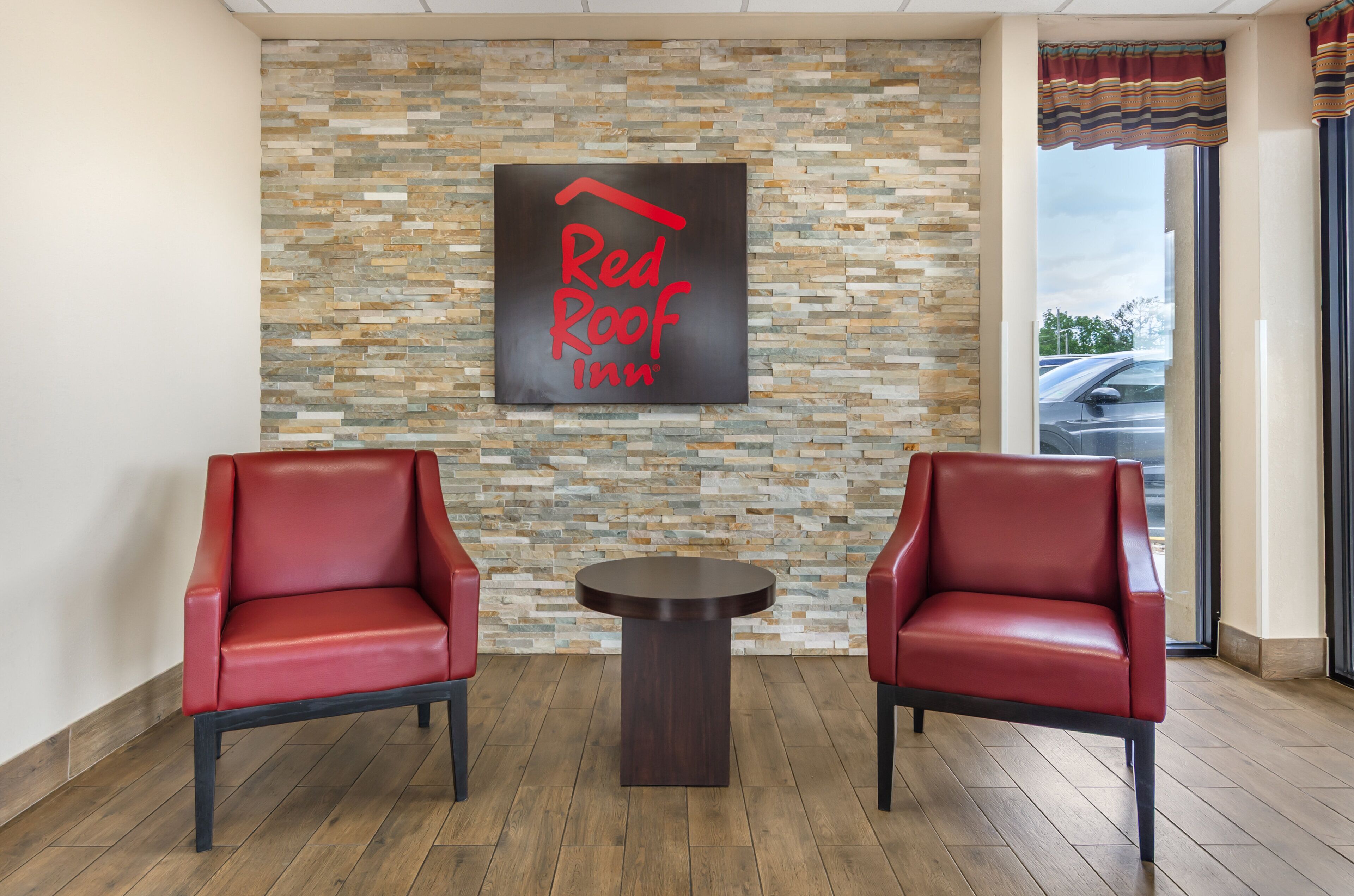 A Red Roof Inn lobby with two red leather chairs, a small round table, and a stone mosaic wall.