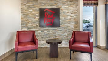 A Red Roof Inn lobby with two red leather chairs, a small round table, and a stone mosaic wall.