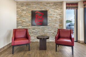 A Red Roof Inn lobby with two red leather chairs, a small round table, and a stone mosaic wall.