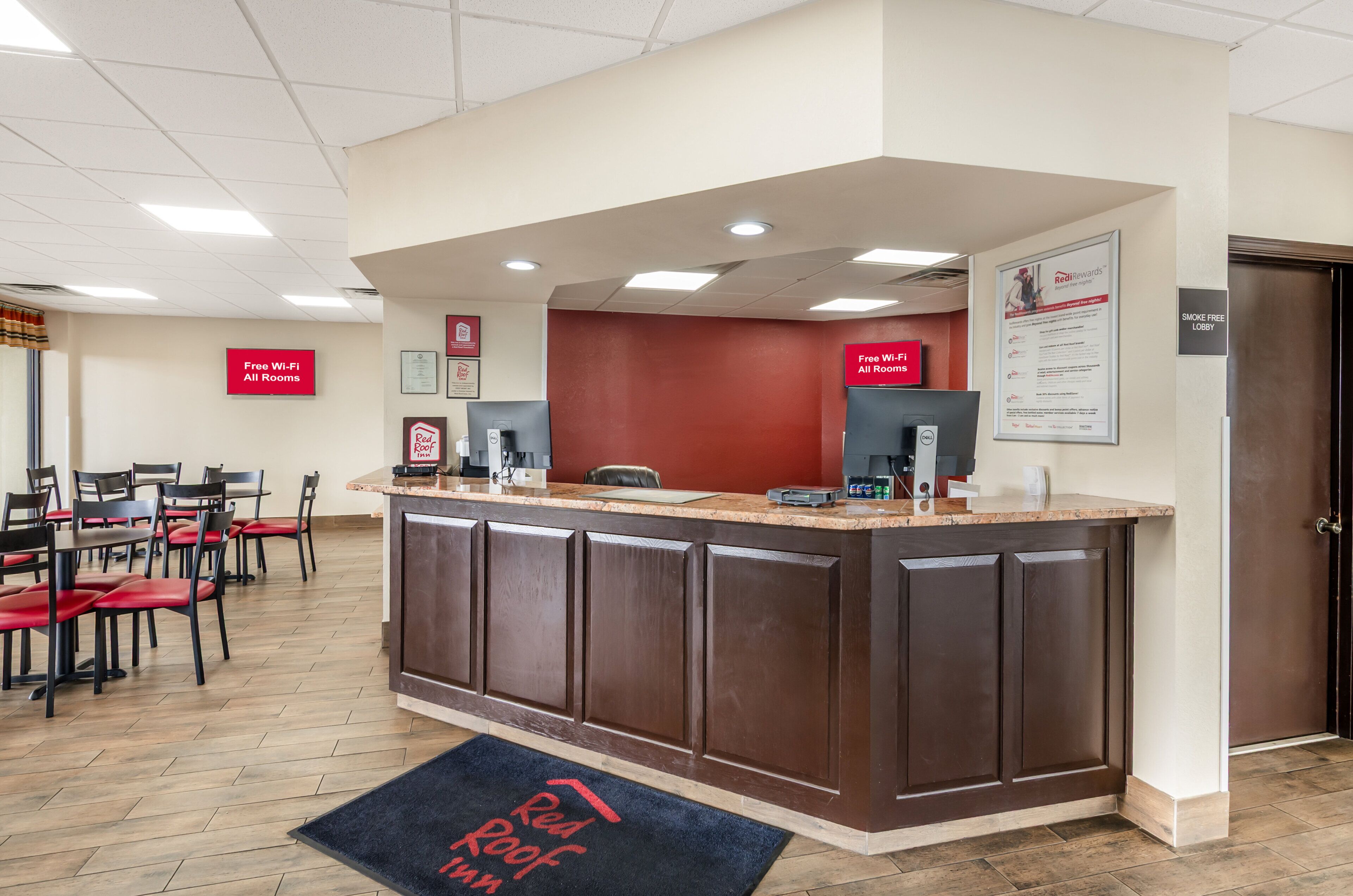 A hotel reception area with a counter, chairs, and a sign indicating free Wi-Fi in all rooms.