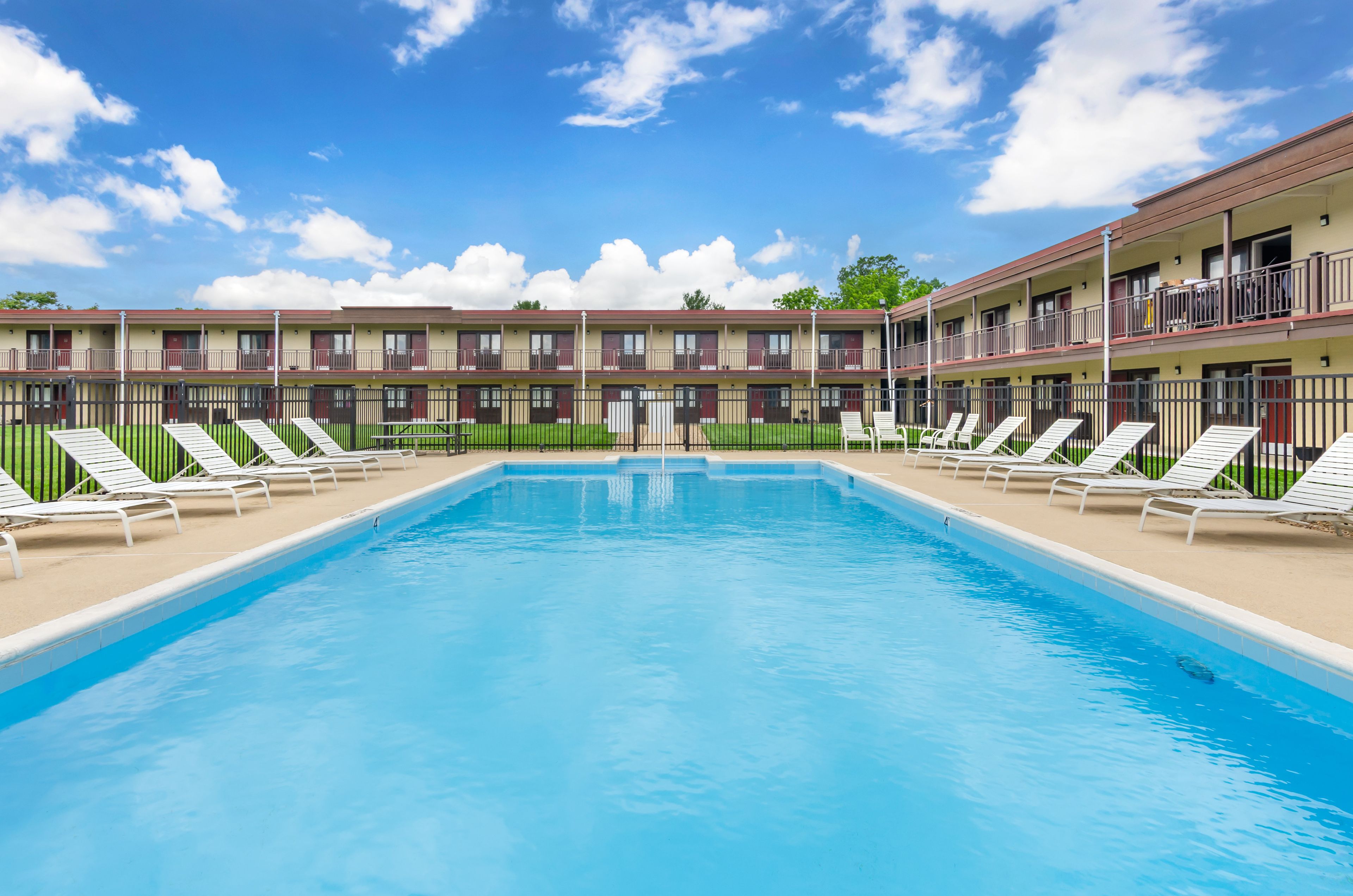 Una piscina con sillones de descanso y un edificio con varios balcones al fondo.