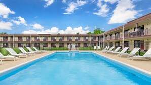 A swimming pool with lounge chairs and a building with multiple balconies in the background. - Red Roof Inn Staunton (Staunton)