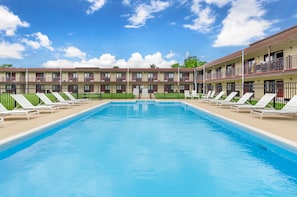 A swimming pool with lounge chairs and a building with multiple balconies in the background. - Red Roof Inn Staunton (Staunton)