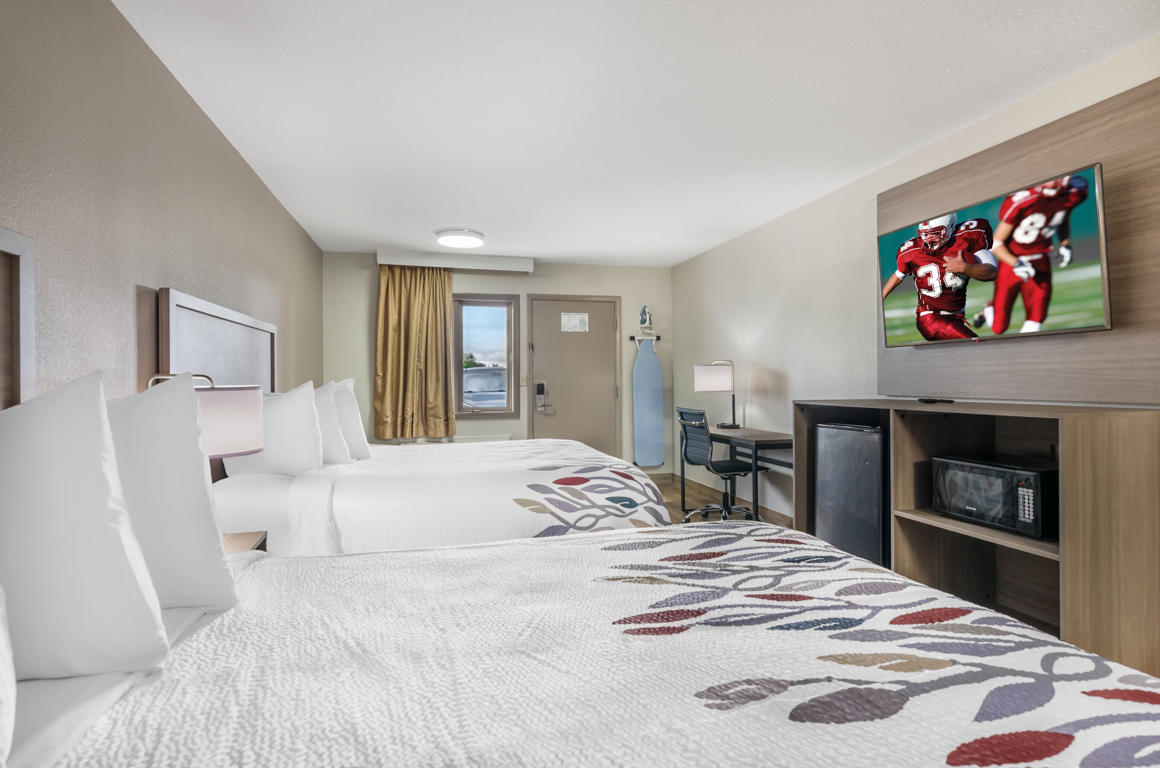 A hotel room with two beds, a desk, a TV, and a minibar.