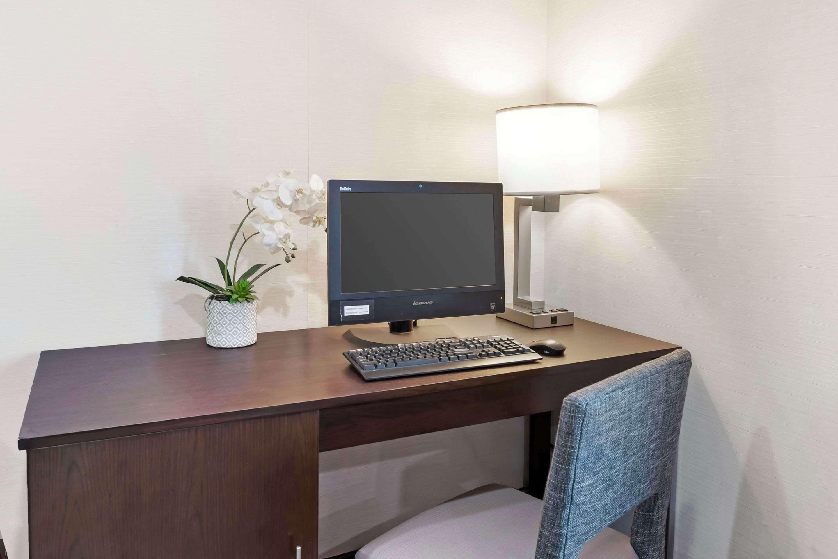 A hotel desk with a Lenovo monitor, keyboard, mouse, and a lamp.