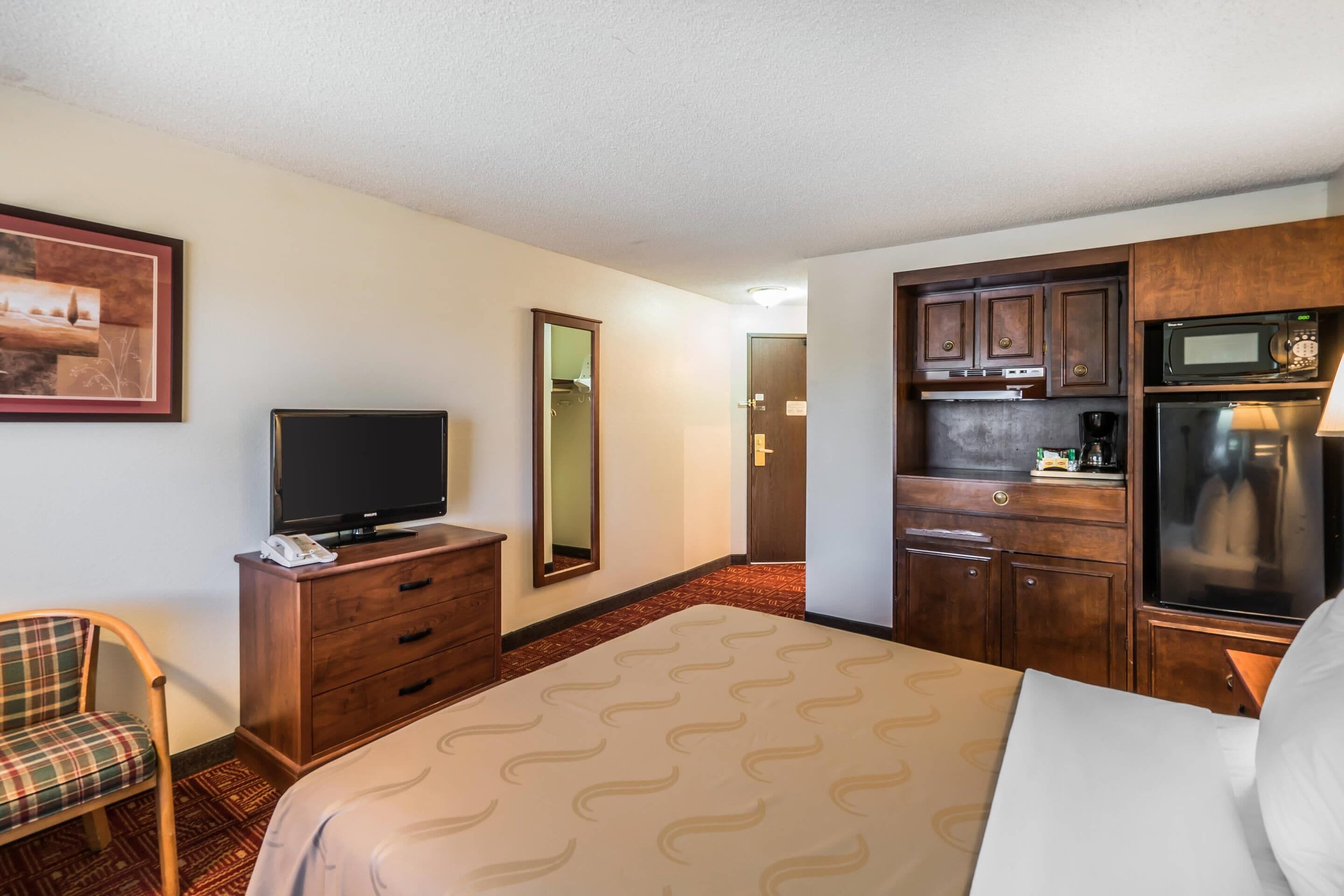A hotel room with a bed, a TV, a desk with a microwave, and a small kitchenette.
