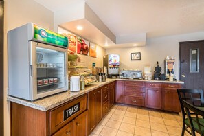 A kitchen with a refrigerator, coffee maker, and a trash bin.