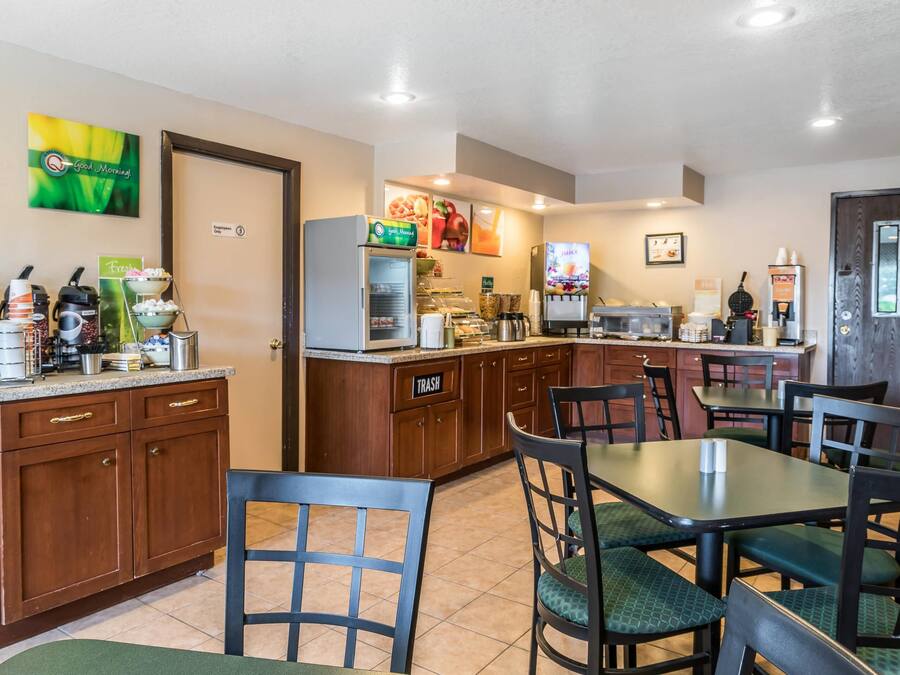 Habitación de hotel con kitchenette, zona de comedor con mesas y sillas, un cesto de basura y un cuadro en la pared.
