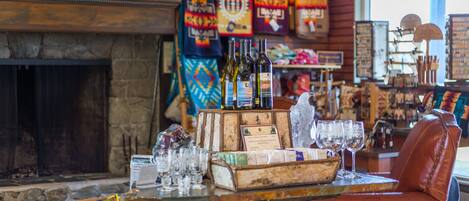 Un intérieur chaleureux avec une cheminée en pierre, des fauteuils en cuir et une table en bois sur laquelle sont disposées des bouteilles de vin et des verres.