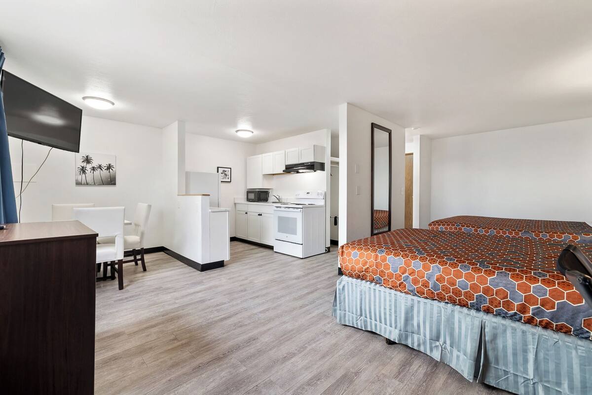 A bedroom with a bed, a desk, and a kitchenette.