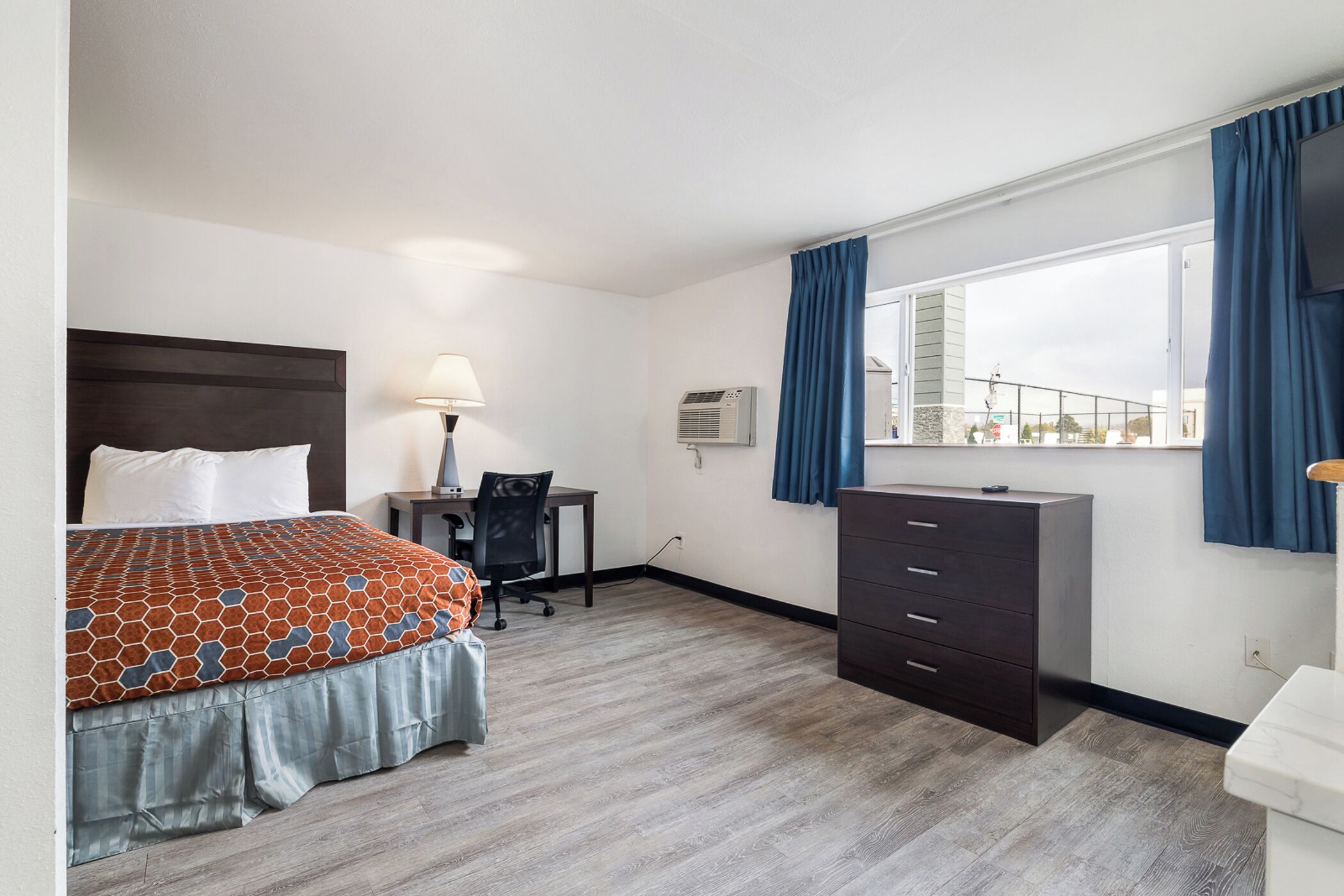 Habitación de hotel con cama, escritorio, silla, cómoda y ventana con cortinas.