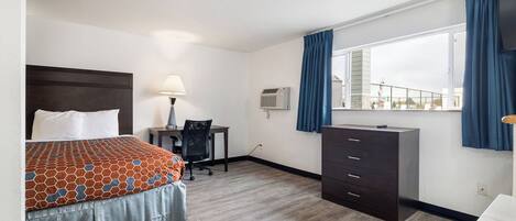 Habitación de hotel con cama, escritorio, silla, cómoda y ventana con cortinas.