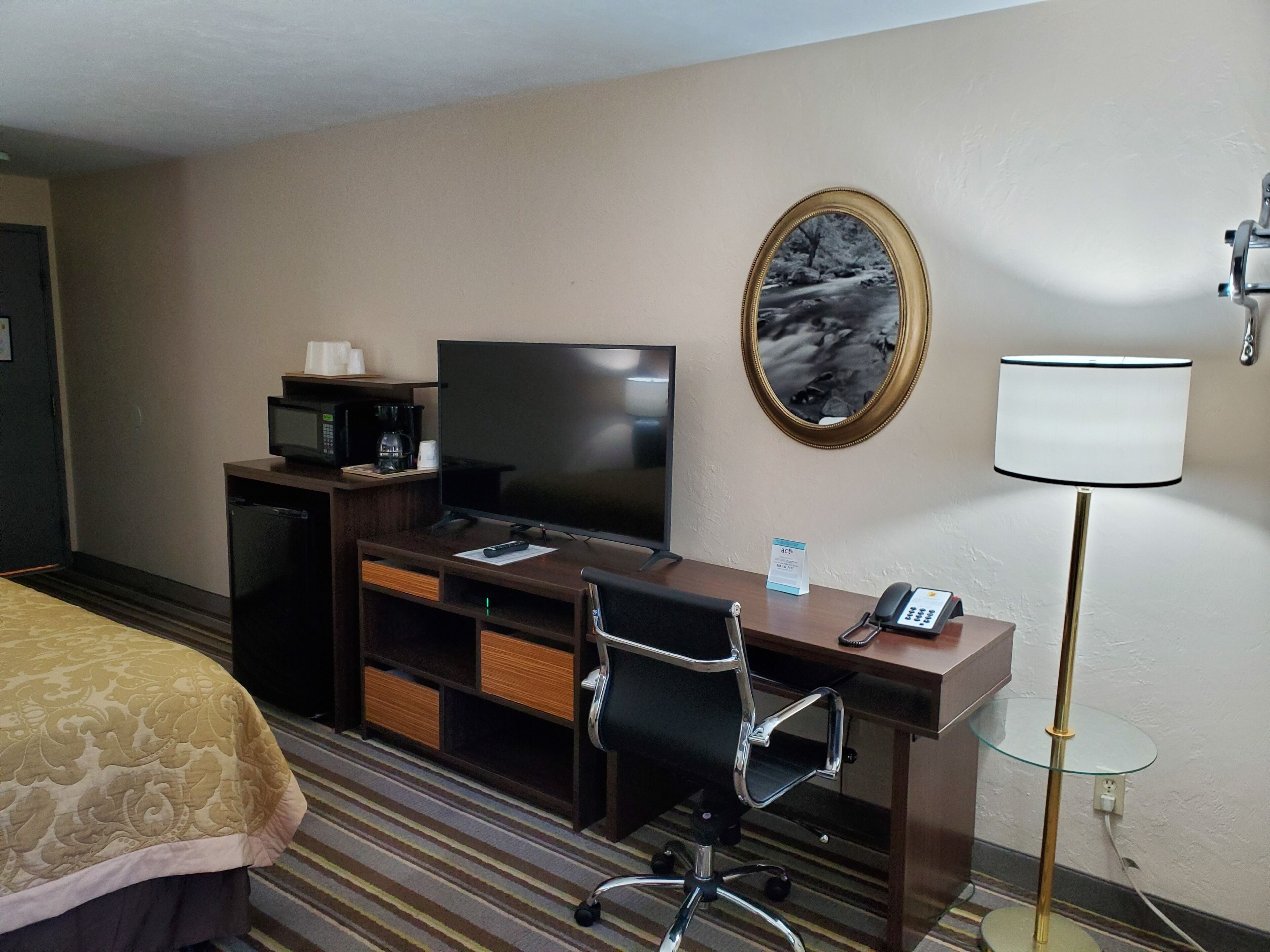 Habitación de hotel con cama, escritorio con televisor, silla, lámpara de escritorio y teléfono.