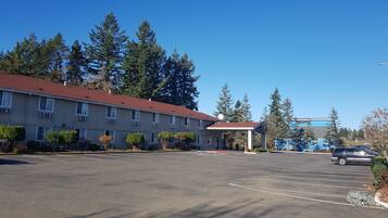 Ein Motel mit rotem Dach, einem überdachten Parkplatz und einer Baumreihe im Hintergrund.