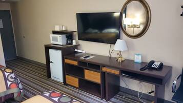 Quarto de hotel com cama, escrivaninha com luminária, telefone, televisão, micro-ondas e geladeira.