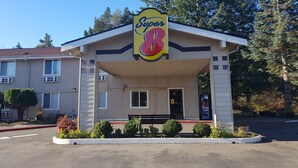 Un motel Super 8 de estructura sencilla y un solo piso, con un acceso cubierto y un pequeño estacionamiento con plantas en macetas.