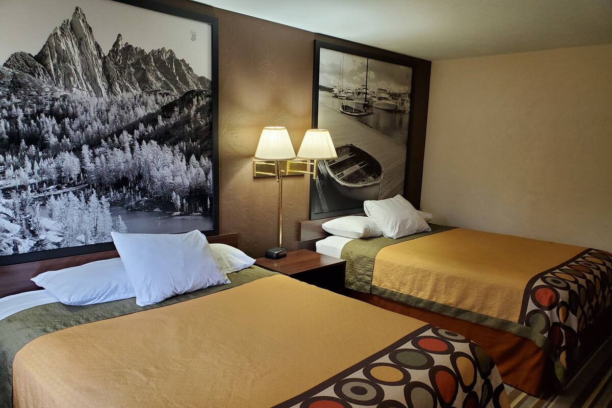 Ein Hotelzimmer mit zwei Betten, einem großen Landschaftsbild von Bergen, einem Bild eines Bootes und einer Lampe.