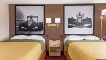 A hotel room with two beds, each with a green and yellow bedspread, a nightstand with a lamp, and two framed pictures of race cars on the wall.