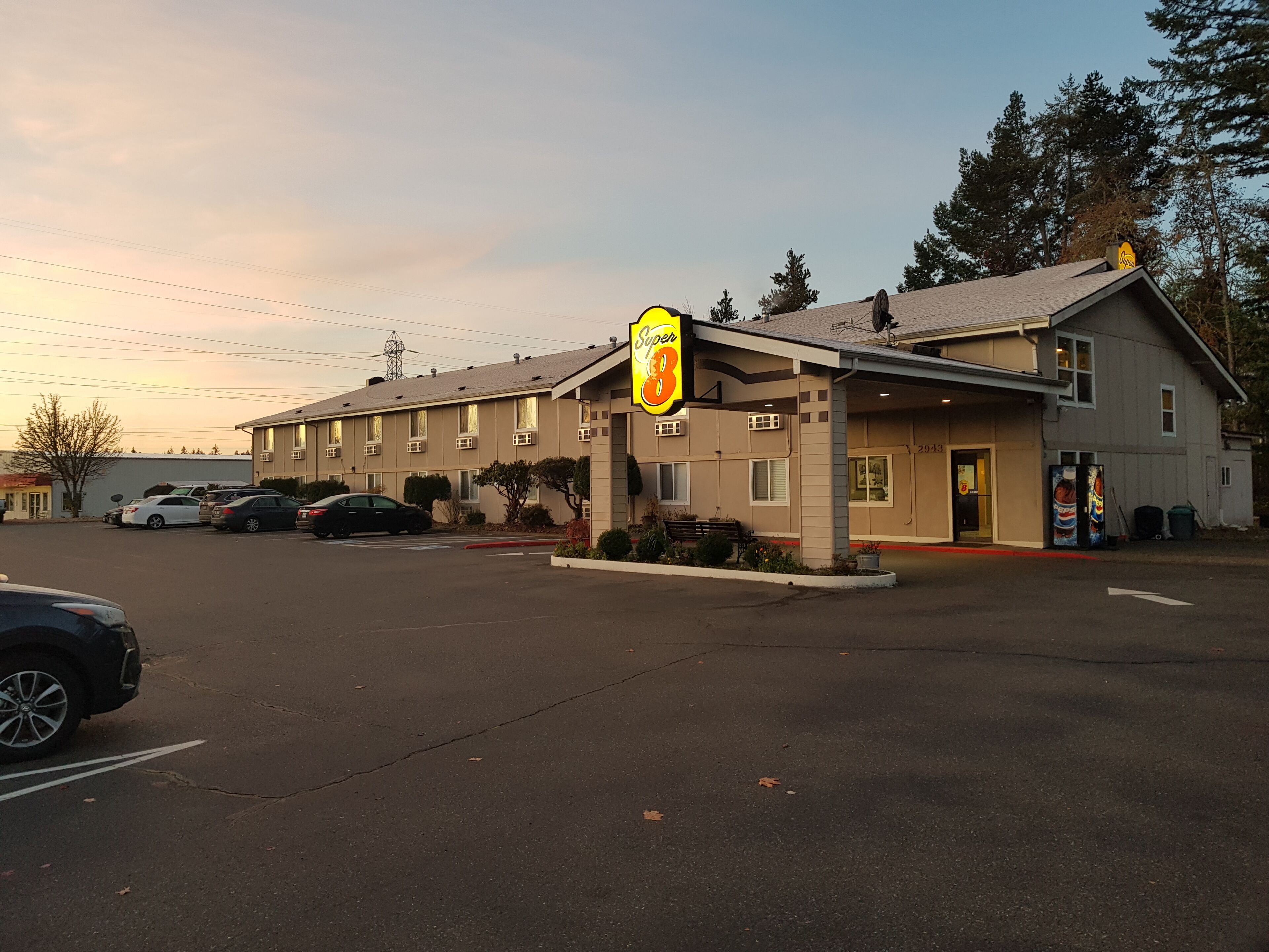 Un motel con el cartel 'Super 8', un estacionamiento y un edificio de fachada color crema.