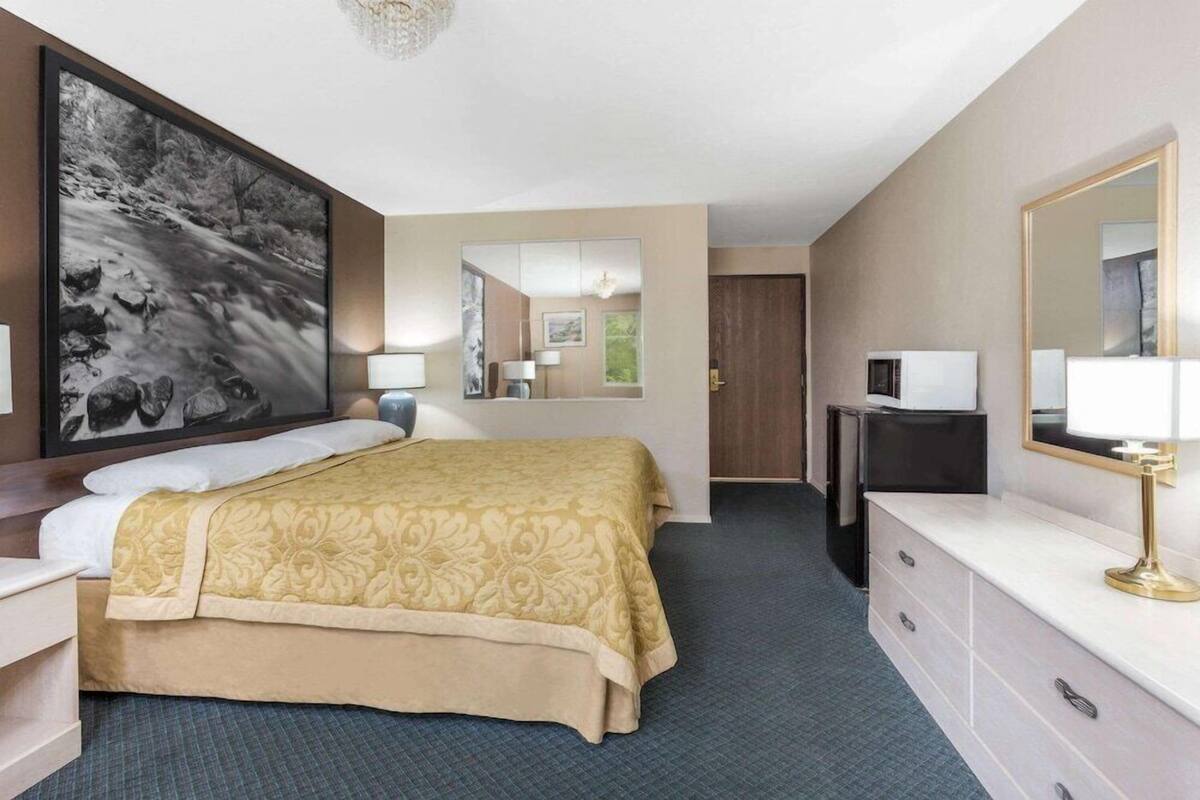 Ein Hotelzimmer mit Bett, Nachttisch, Lampe, Kommode, Spiegel und einem großen gerahmten Bild an der Wand.