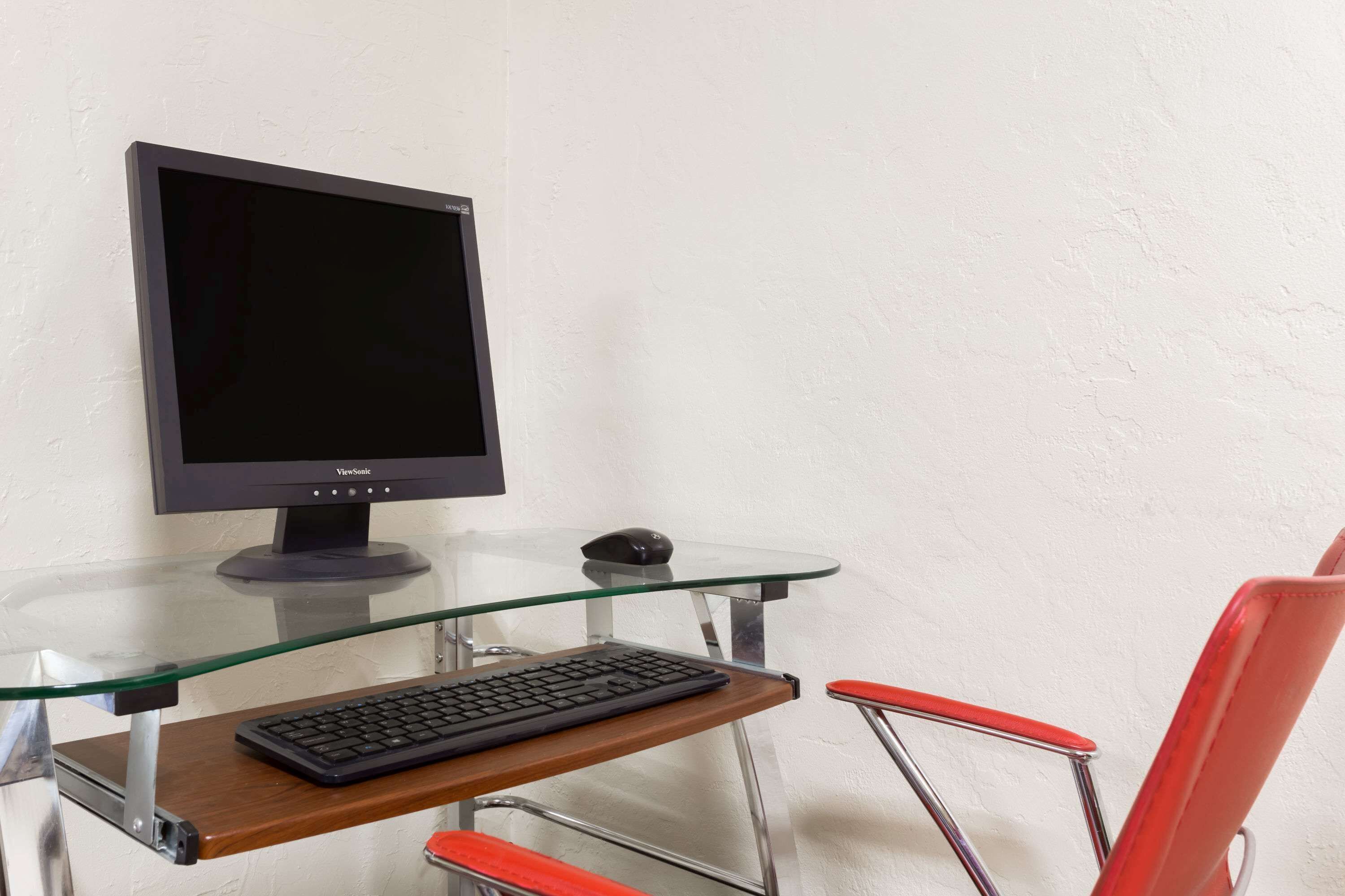 Ein moderner Arbeitsplatz mit einem Glastisch, einem Computermonitor, einer Tastatur und einem roten Stuhl.