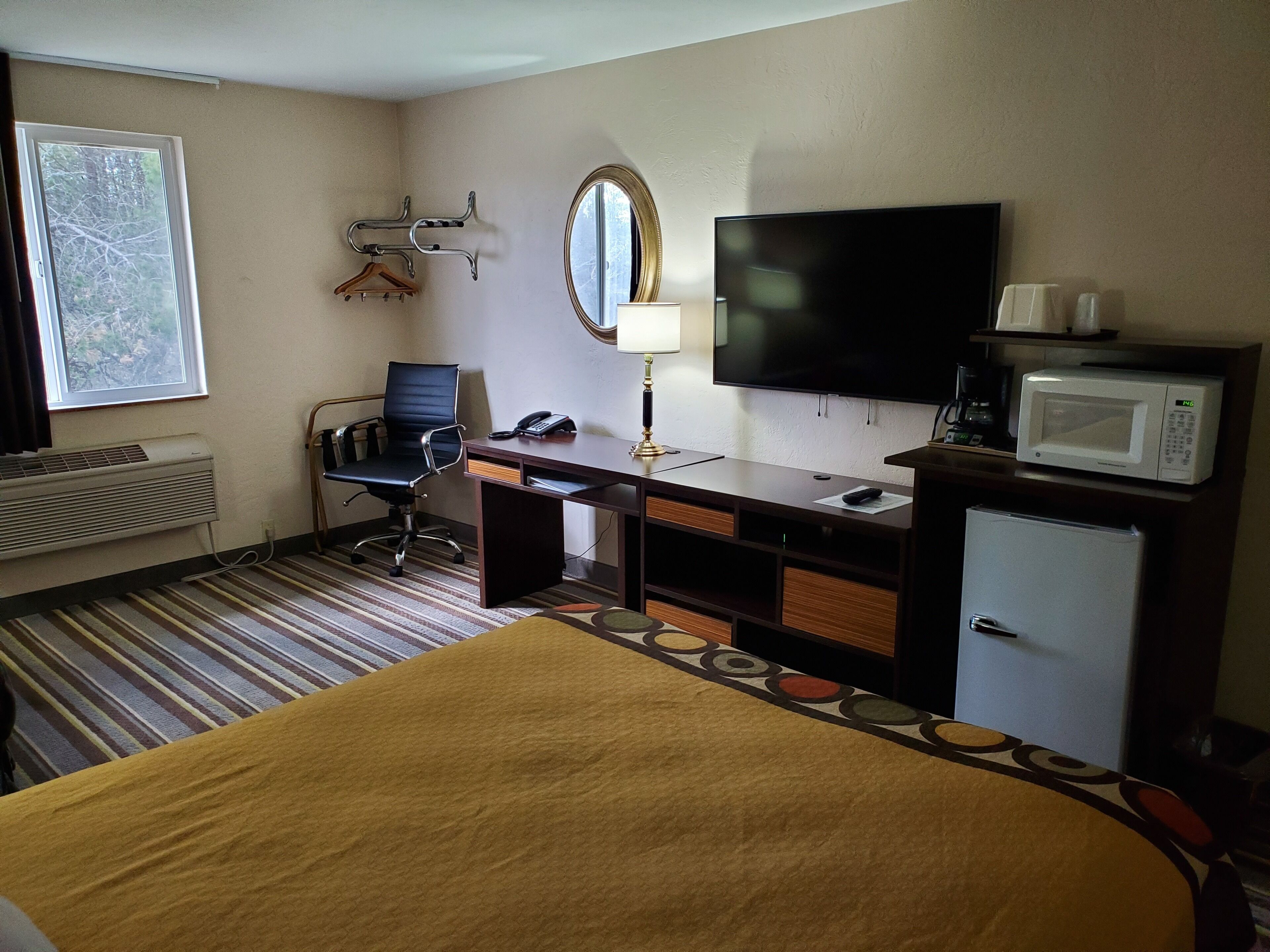 A hotel room with a bed, a desk with a computer, a television, a microwave, and a small refrigerator.