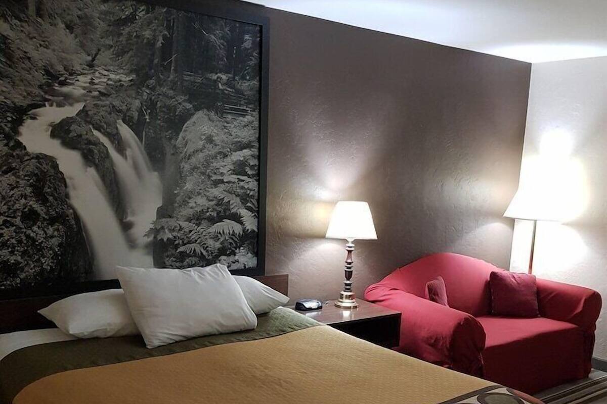 Ein Hotelzimmer mit einem Bett, einem roten Sessel, einem Nachttisch mit Lampe und einem großen Wandbild eines Wasserfalls.