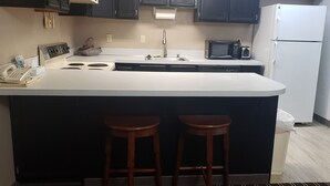 A kitchen with a white countertop, black cabinets, a microwave, a refrigerator, and two wooden stools.