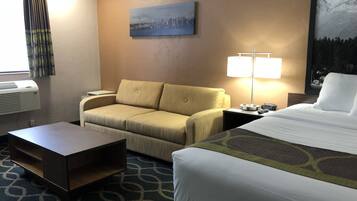 A hotel room with a bed, a sofa, a desk, and a lamp.