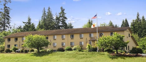 A two-story building with a flat roof, surrounded by a grassy area and trees.