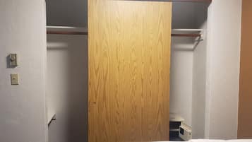 Una habitación con un armario de madera, una pared blanca y un estante pequeño blanco con un microondas.